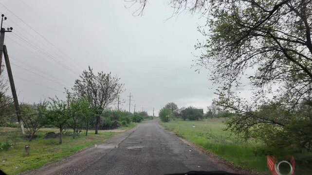 Slow-motion video shot from a moving silver car's perspective on a bumpy asphalt road in the countryside. The car's body 
