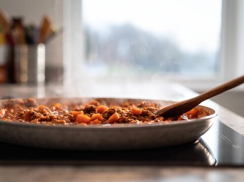 Bolognese ragu with minced meat and diced vegetables simmering in a pan, steam rising, perfect for home cooking and meal preparation