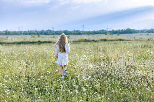 Young girl running away in a wide flowering meadow under a cloudy sky.
