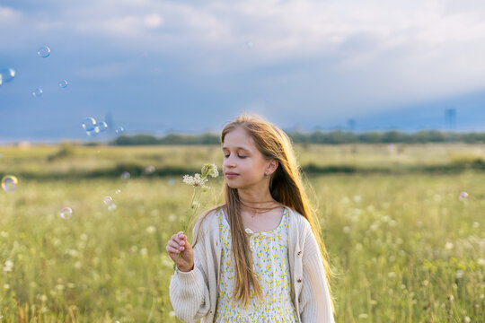 Young girl smelling a wildflower in a green field. Summer aesthetic