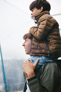 Child on young adult males shoulders looking over a city from building