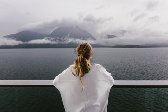 Blond teen girl looking out on balcony of cruise ship at mountains