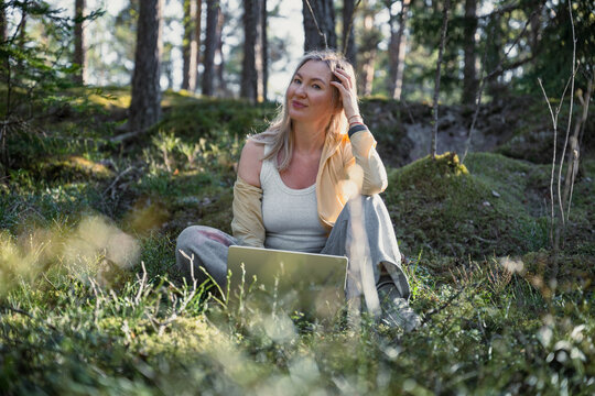 Woman working remotely with laptop in peaceful forest sunlight