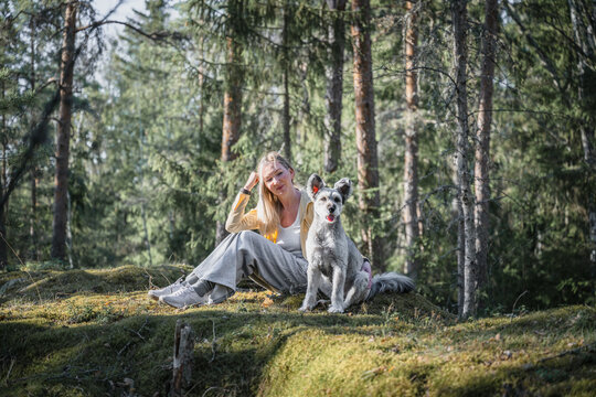 Woman relaxing with playful dog on mossy hill in forest sunlight