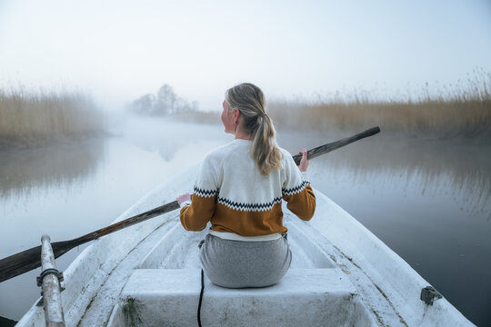 Woman rowing boat through misty river at peaceful sunrise