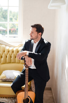Handsome man in suit laying at guitar while sitting on sofa hotel