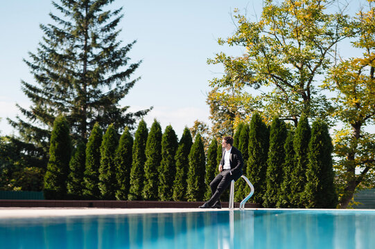 Handsom groom sitting on the edge of a swimming pool and looking away
