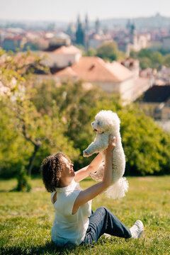 Woman holds Bichon Frise dog in park with Prague skyline background