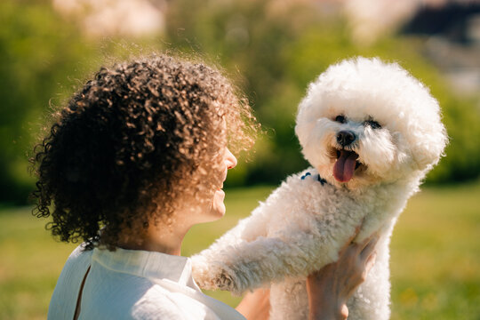 Curly Woman interacts with Bichon Frise dog in park setting in Prague
