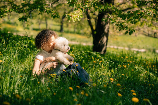 Woman enjoys time with Bichon Frise dog in park during spring day