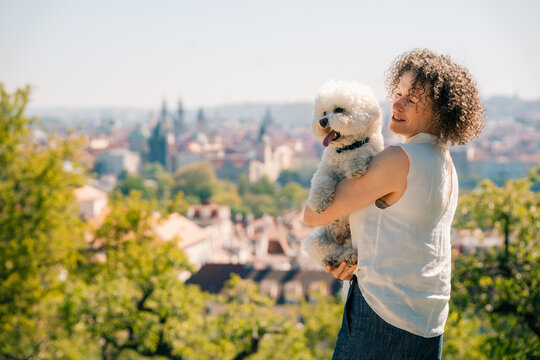 Woman holds Bichon Frise dog while overlooking Prague city view