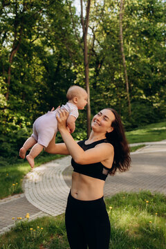 Happy mother lifting baby outdoors in park during fitness workout