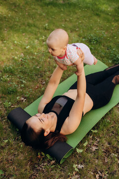 Happy mother exercising with baby on yoga mat outdoors