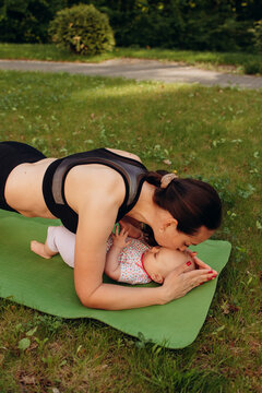 Mother kissing baby during outdoor workout on yoga mat