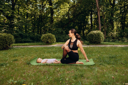 Mother and baby relaxing on yoga mat outdoors in park