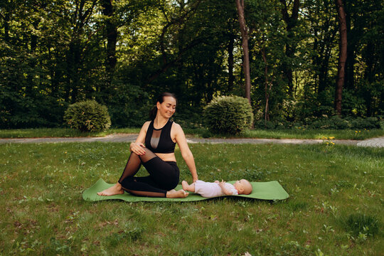 Young mother relaxing with baby on yoga mat in park
