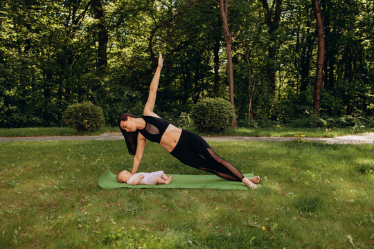 Mother practicing side plank yoga pose near baby outdoors