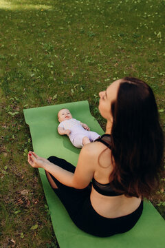 Mother meditating near baby on yoga mat outdoors