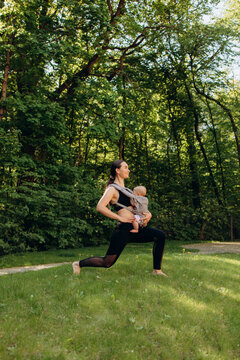 Sporty mother exercising with baby carrier outdoors in park