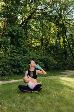 Active mother drinking water while holding baby outdoors
