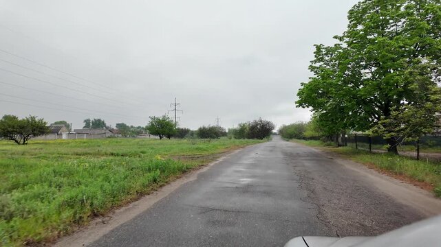 Slow-motion video shot from a moving silver car's perspective on a bumpy asphalt road in the countryside. The car's body 