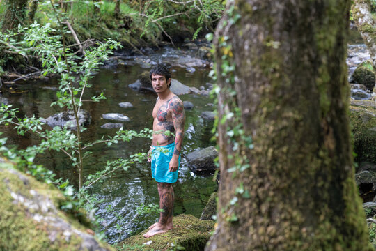 Tattooed man standing by a natural forest river