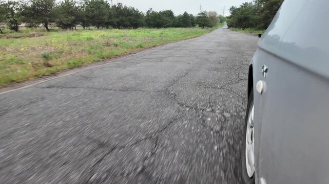 Slow-motion video shot from a moving silver car's perspective on a bumpy asphalt road in the countryside. The car's body 