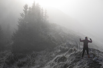 Obraz premium Woman Hiker Celebrating On Foggy Frosty Mountain Ridge At Sunrise With Backpack And Raised Arms