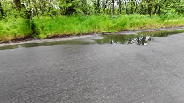 Slow-motion video shot from a moving silver car's perspective on a bumpy asphalt road in the countryside. The car's body 