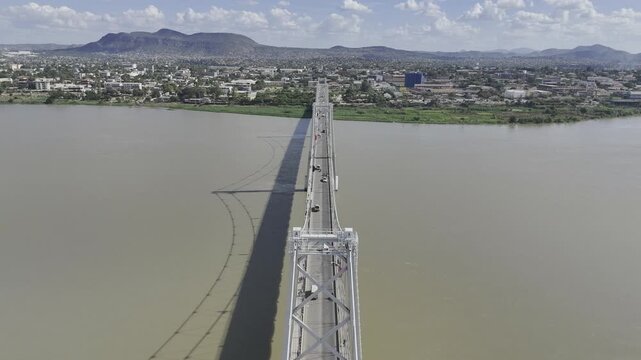 Drone facing southwest flies backwards from Samora Machel Bridge over Zambezi River on a sunny day in Tete, Mozambique