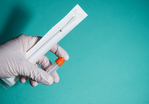 Close-up of gloved hand holding laboratory sample tube and sterile swab kit against blue background. Concept of DNA testing, medical diagnostics, laboratory research and healthcare analysis