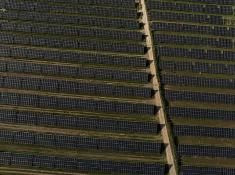 Aerial view of a large solar farm with rows of photovoltaic panels and a dirt path in Priolo Gargallo, Sicily, Italy.