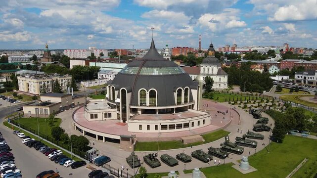 Aerial cinematic orbit shot of the Tula State Museum of Weapons, known for its unique helmet-shaped architecture, and the outdoor military equipment exhibition. A panoramic view of Tula city center un