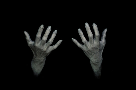 Bony pale and sinewy male hands with long nails reach up out of the total darkness. Dark and creepy supernatural atmosphere.