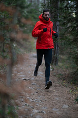 Obraz premium Man Running Trail In Red Jacket On Forest Path During Cold Weather Outdoor Workout