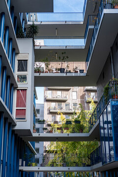 Inside a Rive Gauche courtyard in Paris, apartment balconies and walkways cross above shaded windows and planted open levels in clear air.