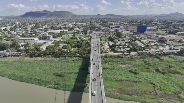 Drone flies southwest from middle of Samora Machel Bridge over Zambezi River to downtown on a sunny day in Tete, Mozambique