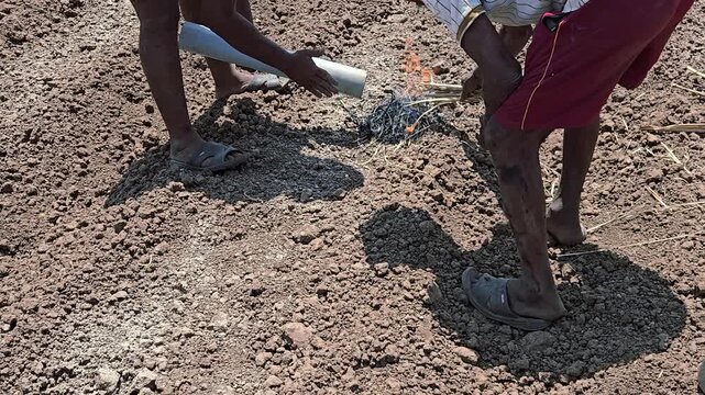 Farmers and plumbers heat a PVC pipe over a small foliage fire to soften it for an irrigation joint. In harsh sunlight, they repair a field leakage, manually expanding the pipe for a connection.