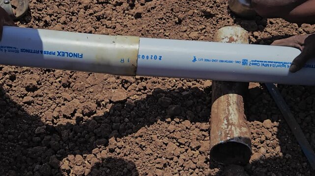 Workers in a field join two PVC pipes for an irrigation line. After heating the pipe ends, they carefully fit them together to ensure a leak-proof connection, securing a vital water supply for crops.