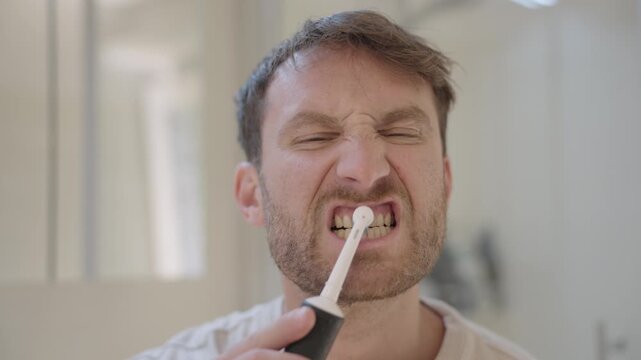 Man with a beard brushing his teeth with an electric toothbrush during his morning routine