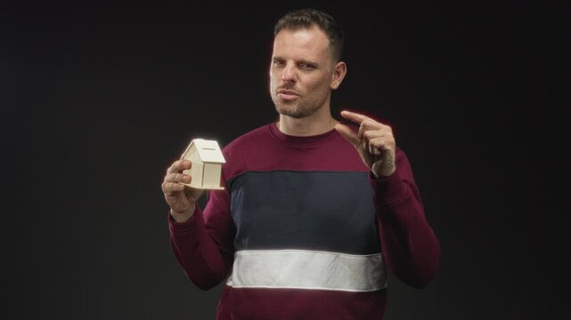 Man holding miniature wooden house and pinching a tiny gap with fingers in studio; doubt financial risk.