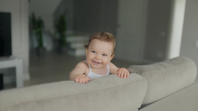 Giggling baby girl leaning on couch backrest in a bright room