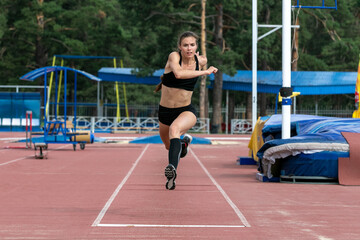 Fototapeta premium Beautiful female athlete triple jump in training at stadium