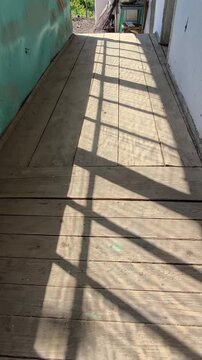 Vertical video of an old porch in Comarna, Iasi. Dramatic window shadows on a weathered, rustic wooden deck of a dilapidated traditional house. Dramatic window shadows on a weathered, rustic wooden de
