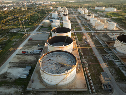 Aerial view of large industrial storage tanks and refinery infrastructure surrounded by green fields in Augusta, Sicily, Italy.