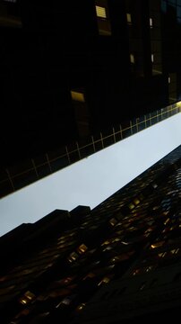 Bright lights from windows of tall buildings create reflections on the surrounding structures at night. The urban scene shows different heights and angles of the buildings.
