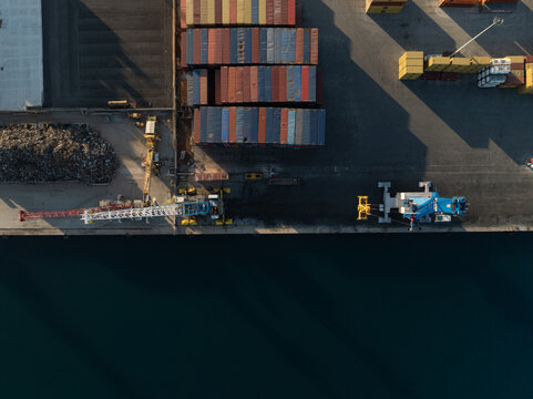 Aerial view of colorful shipping containers and industrial cranes at the port during sunset in Augusta, Sicily, Italy.