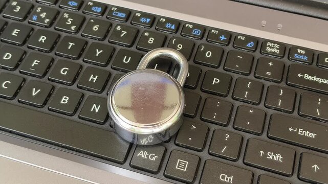 Closeup of hand put padlock on laptop computer keyboard. Tech device privacy, system security and user data safety concern. Cybercrime, cyberattacks, online scams in technology business concept.