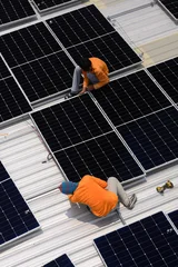 Workers are inspecting the system and installing solar panels for clean energy. Solar panels on the factory rooftop (PHOTO). © eakarat