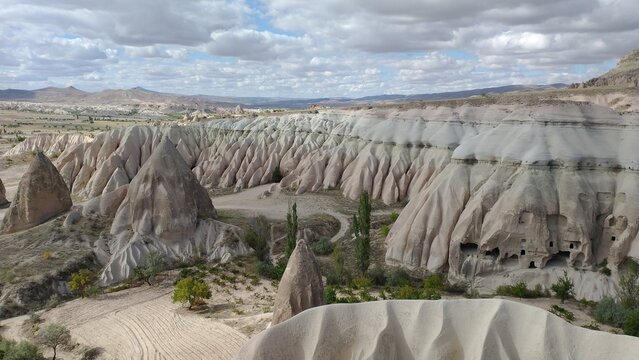 Panoramic view of eroded volcanic tuff landscape with fairy chimneys and ancient rock-cut structures in Cappadocia, Turkey.